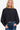 Woman wearing a black asymmetric hem sweater with long sleeves, styled casually with jeans.